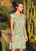 Woman stands in green based floral print cotton dress with pin tucks across the bodice that lead to a slight A-line skirt