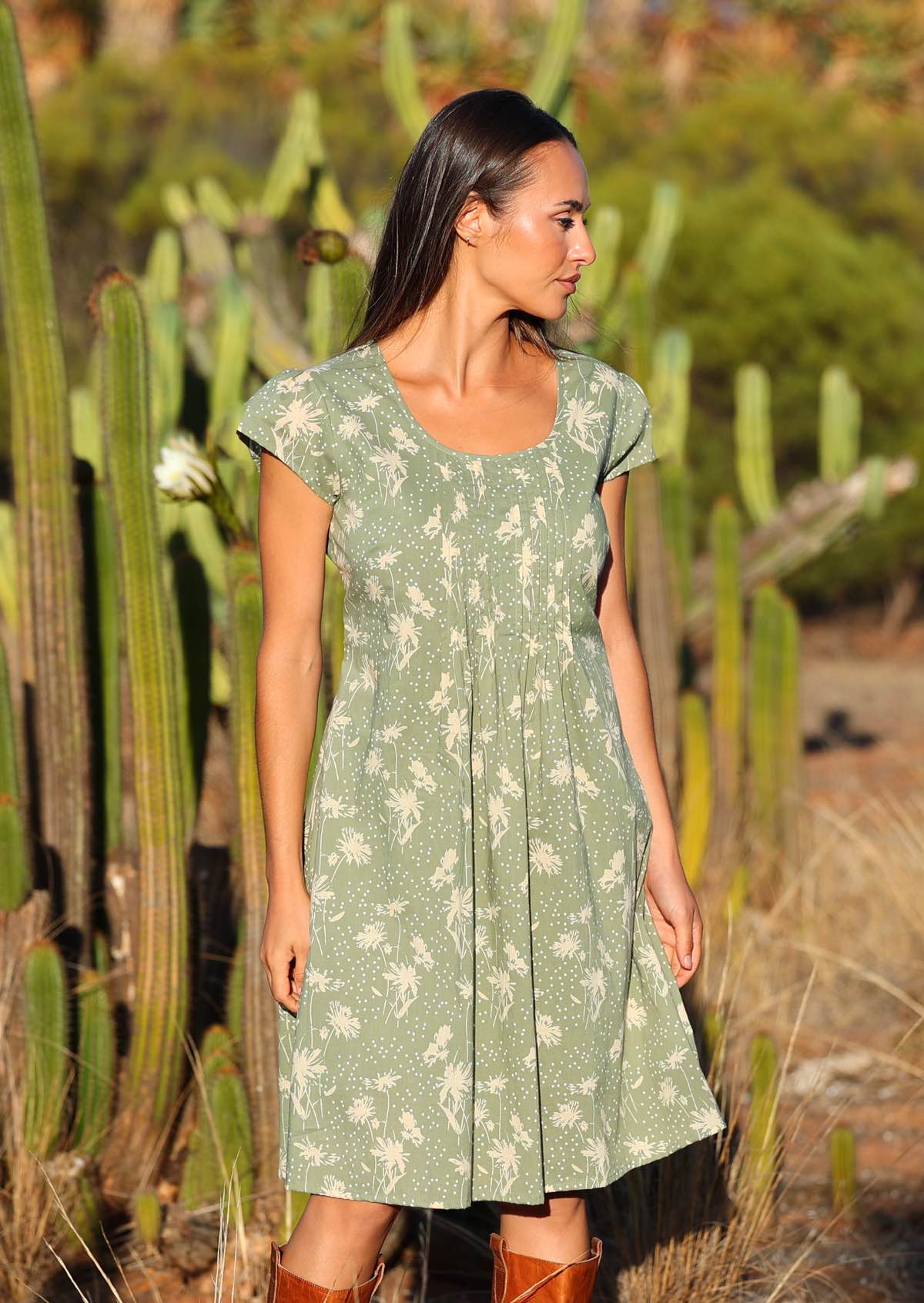 Woman wears cotton knee length dress with deep round neckline and cap sleeves, in pale green and cream floral print