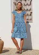 Woman wearing a blue floral cotton knee length dress with cap sleeves and a round neckline