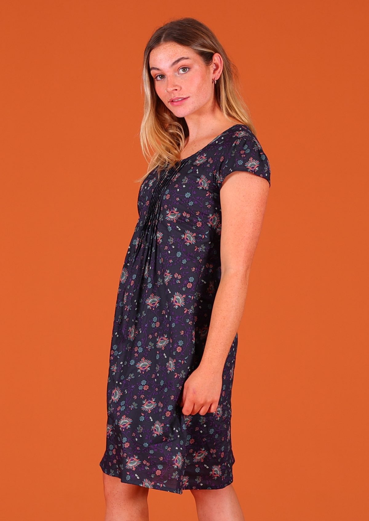 Model standing side on wearing 100 percent cotton short sleeve pleated sundress in deep purple Indian floral