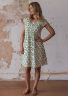 Woman poses in cotton cap sleeved above knee dress with yellow and green floral print on a white base