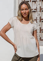 Woman wearing a natural white 100% cotton cap sleeve top with scoop neck