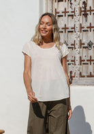 Woman wearing a natural white top and olive green pants standing in front of a decorative door.