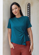 Woman wearing a teal rayon t-shirt with twist detail on the left hip, paired with rust pants