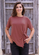 Woman wearing a terracotta short sleeve rayon top and black pants with hand in pockets