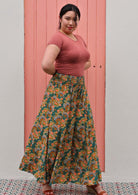 Woman in green wide legged floral pants with shirred elastic waist and pink scoop neck tee in front of pink door