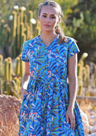 Close up of woman standing in blue cotton leafy button down maxi dress with one hand in pocket 