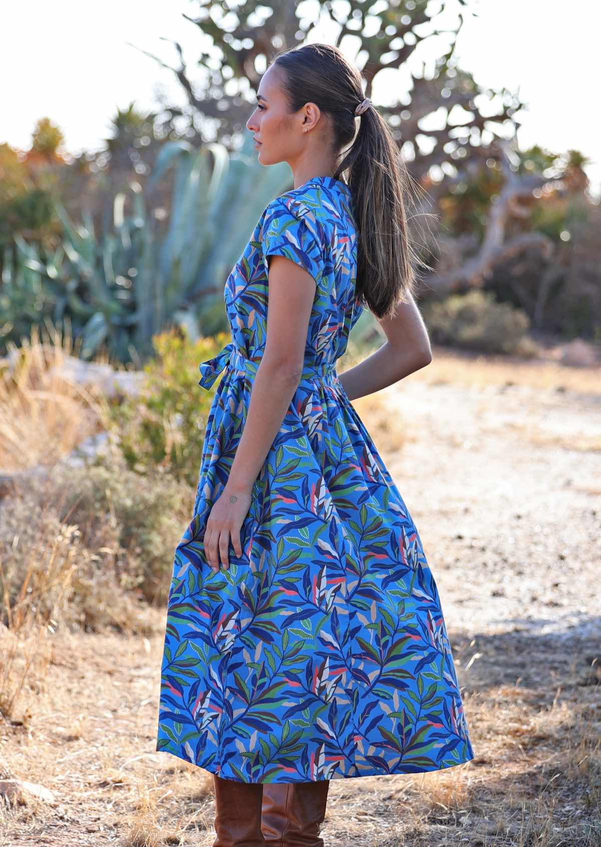 Side view of woman standing in blue cotton leafy button down maxi dress with one hand in pocket 