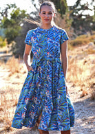 Woman standing in blue cotton leafy maxi dress with Mandarin neck collar and one hand in pocket 