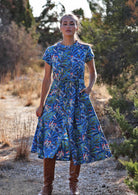 Woman standing in blue cotton leafy button down Mandarin collar maxi dress with one hand in pocket 