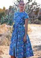 Woman standing in blue cotton leafy button down maxi dress with Mandarin collar and waist tie