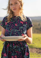 woman in navy cotton dress holding stack of plates