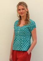 Model with one hand on in pant pocket wearing 100 percent cotton top in aqua with small functional shell buttons