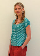 Model with one hand on in pant pocket standing to the side wearing 100 percent cotton top in aqua with small functional shell buttons