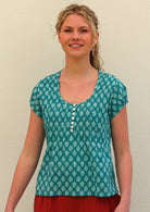 Model smiling wearing 100 percent cotton top in aqua with small functional shell buttons