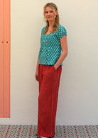 Model with one hand on in pant pocket standing to the side wearing 100 percent cotton top in aqua with small functional shell buttons paired with wide leg pants