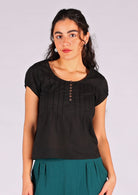 Model poses in 100% cotton black cap sleeved top with scoop neckline