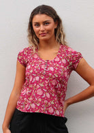 Model poses in floral print cotton cap sleeve top with scoop neckline and buttons down front centre