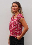 Woman stands sideways in cotton cap sleeve floral print top with decorative pin tucks across chest