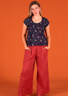 Model standing with hands in pant pockets wearing 100 percent cotton blouse dark purple paired with wide leg pants Jaya Marsala