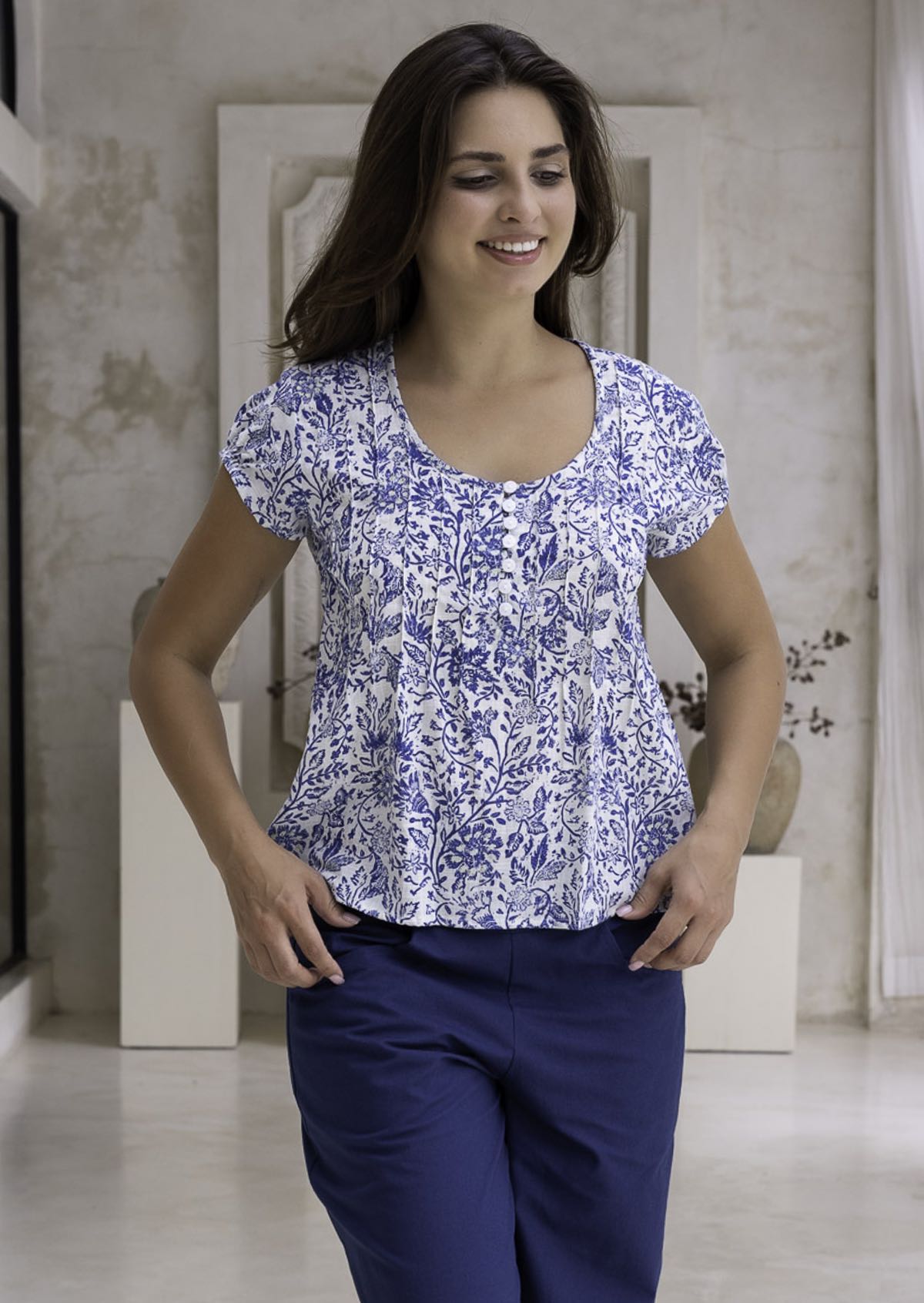 Woman wearing a white based blue floral print cotton top with coconut buttons.