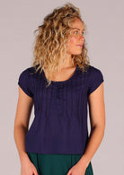 Model wears 100% cotton dark blue cap sleeved top with scoop neckline and small pleats across chest