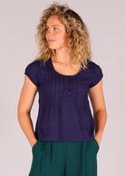 Model wears blue cotton top featuring a flattering scoop neck and delicate pin tucks across the chest, accented with small buttons