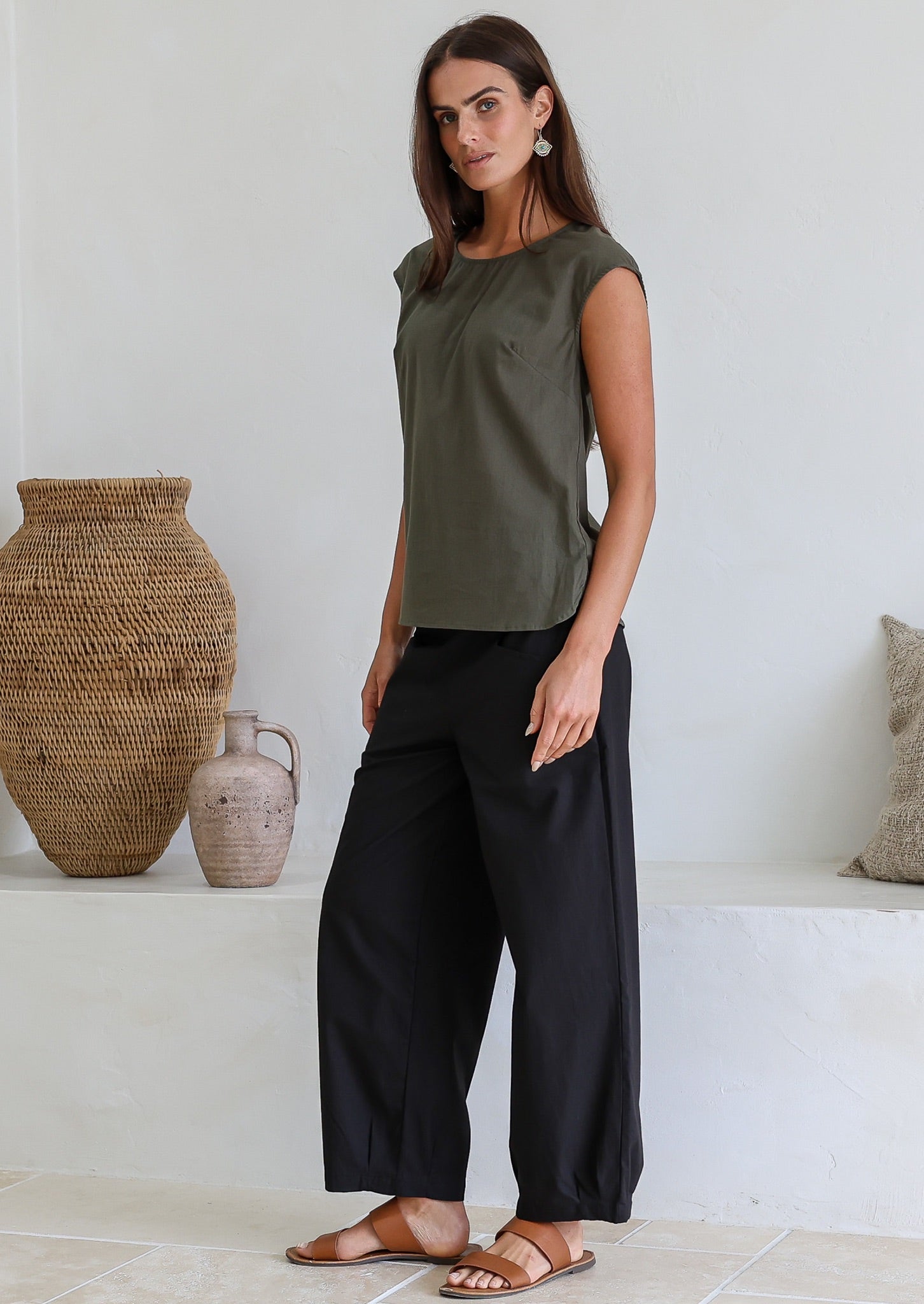 Woman wearing an olive green 100% cotton sleeveless top paired with black cotton pants