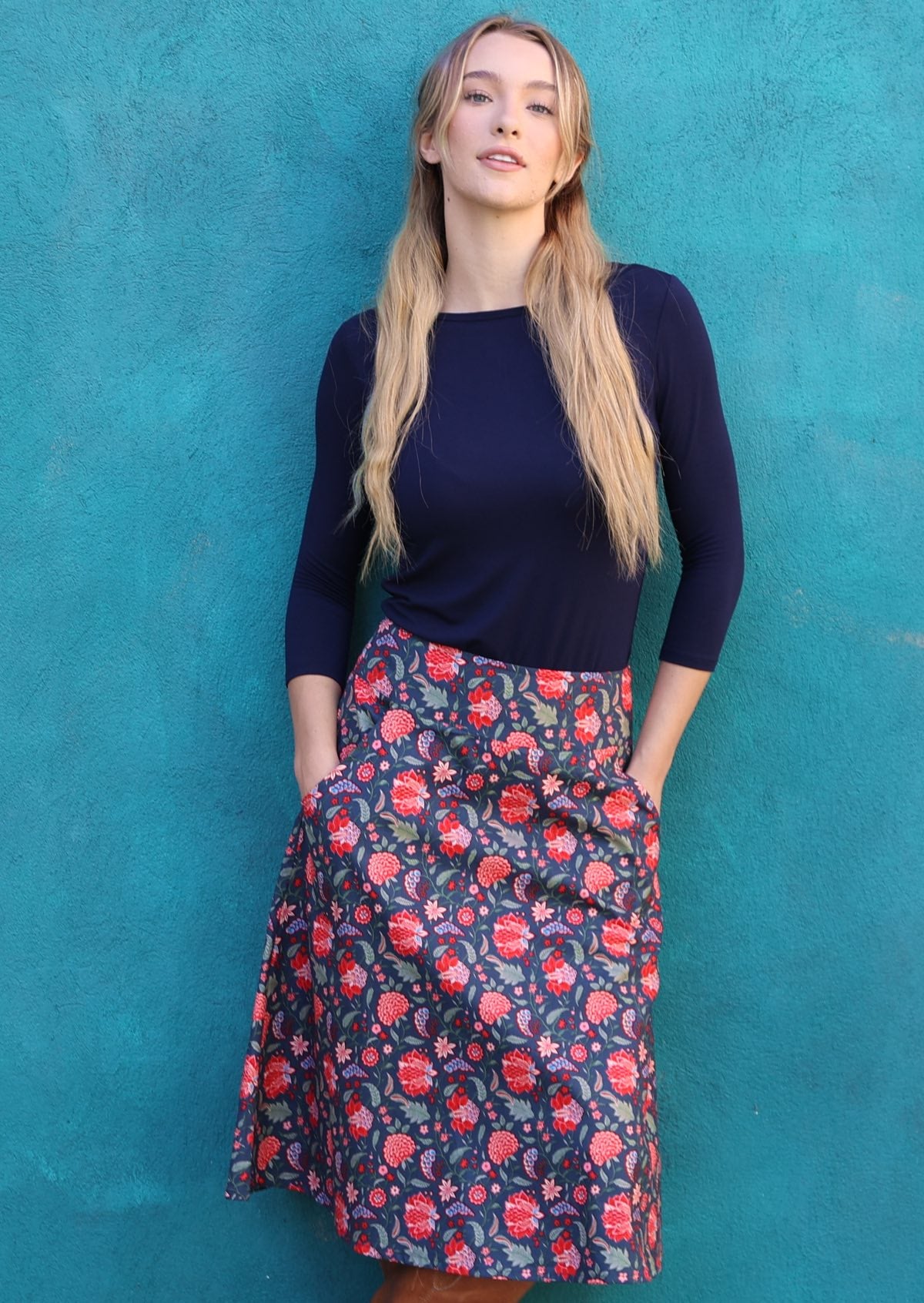 Model wearing 100% cotton A line skirt with beautiful red floral print and hands in the pockets.