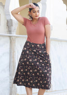 Model wears black floral printed, knee length cotton skirt with side zipper and hand in pocket.