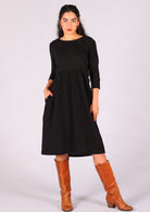 Model strikes a pose in black double cotton relaxed fit dress with hand in pocket