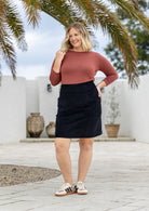 Woman wearing a dusty pink top, cotton corduroy knee length black skirt, and sneakers.