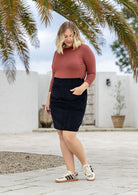 Woman in a cotton corduroy black A-line skirt with her hands in pockets, paired with a dusty pink top 