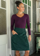 woman wearing a cotton corduroy skirt and basic top standing indoors with one hand in pocket