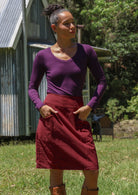 Woman wearing cotton corduroy skirt in deep, luxurious, and intense red-purple hue with both hands in pockets
