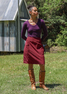 Woman standing outdoors wearing a basic top and corduroy skirt with brown boots.