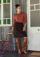 Woman wearing a aalia corduroy skirt in ganache standing in front of a door with a red chair.