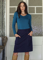 woman wearing a cotton corduroy skirt in  deep, rich, and slightly muted navy blue with both hand in her pockets