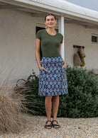 Woman stands in 100% cotton above knee length A-line skirt with piped detailing, pockets and a side zipper.