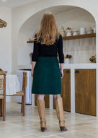 Woman standing backwards wearing a cotton corduroy skirt in deep green shade paired with a basic black top. 