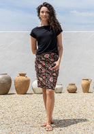 Woman wearing a black top and dark floral cotton skirt standing outdoors with vases in the background