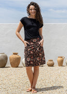 Woman in black top and black based floral cotton skirt with her hands in pockets