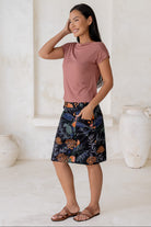 Woman posing slightly sideways wears 100% cotton A-line skirt in black based botanical print, paired with dusty rose basic top.
