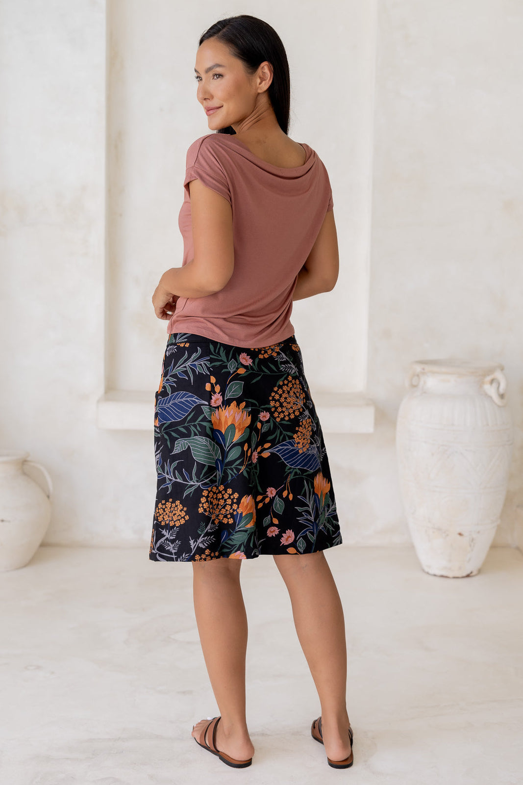 Model posing in a basic pink top and above knee length a-line cotton skirt in black based botanical print with side zipper and pockets