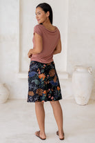 Model posing in a basic pink top and above knee length a-line cotton skirt in black based botanical print with side zipper and pockets