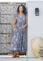 Woman stands in rayon maxi dress with V-neckline and buttoned bodice and hidden side pockets