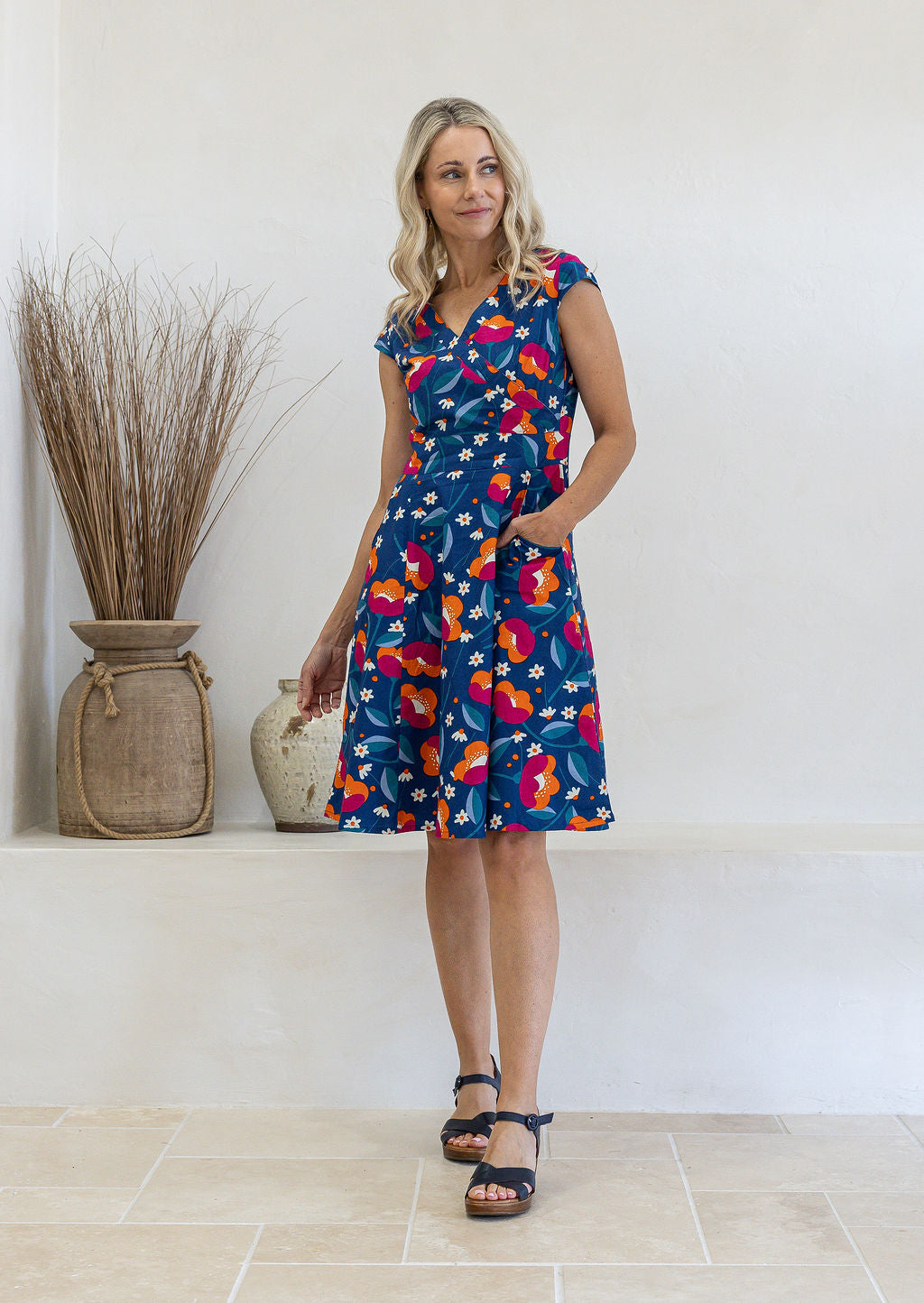 Model is wearing a 100% cotton dress in royal blue based floral print with cap sleeves and pockets