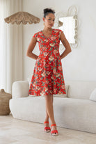 Woman wearing retro inspired cotton knee length dress in vibrant red backdrop featuring elegant multicoloured floral vines.