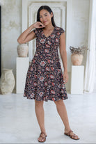 Model wears knee length, retro style black floral cotton dress with crossover bodice, cap sleeves and pockets.
