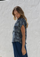 Woman wearing a floral cotton top with short folded cuff sleeves, collar and V neckline